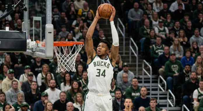 NBA 경기에서 수비수 위로 파워풀한 덩크를 시도하는 스타 포워드 선수